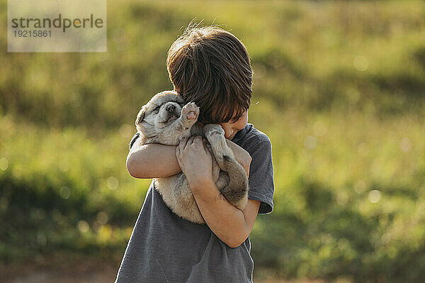 Boy embracing cute mixed breed puppy at meadow