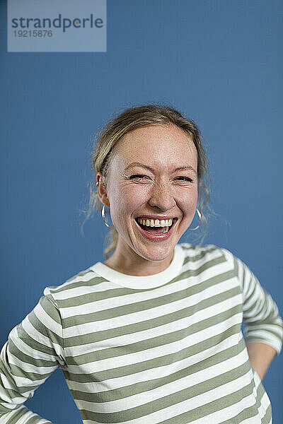 Cheerful woman wearing striped t-shirt laughing against blue background