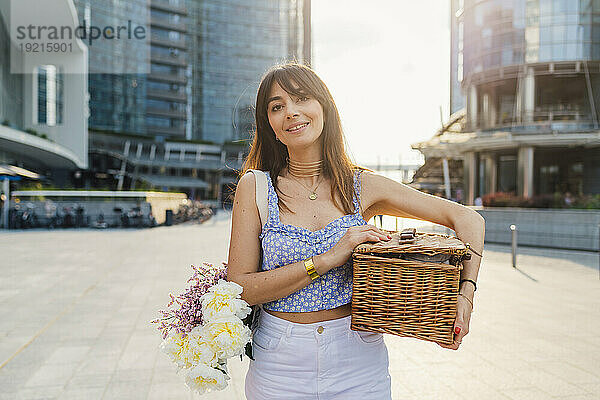 Lächelnde Frau mit Blumenstrauß und Korb an einem sonnigen Tag