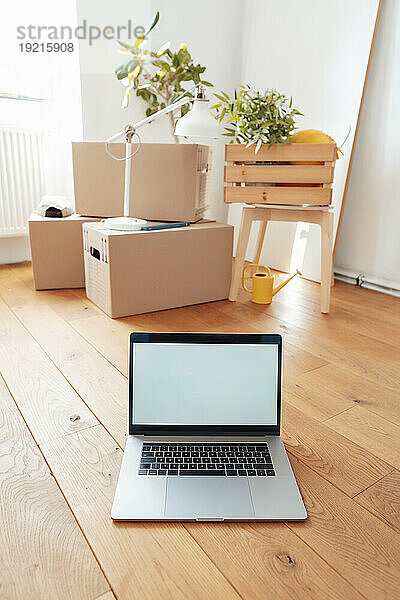Laptop mit Kartons auf dem Boden zu Hause
