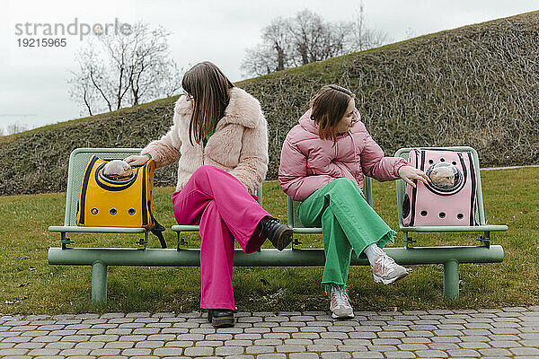 Zwei junge Frauen sitzen neben Katzen in Transportboxen im Park