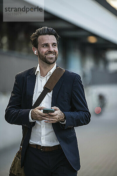 Lächelnder Geschäftsmann mit Mobiltelefon auf Fußweg