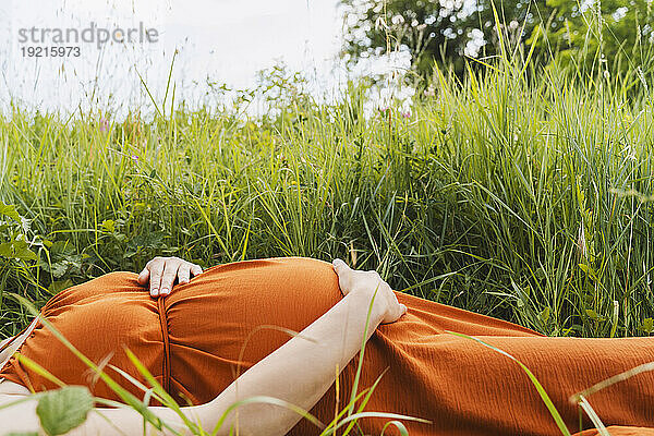 Schwangere Frau liegt in der Nähe von Gras auf der Wiese