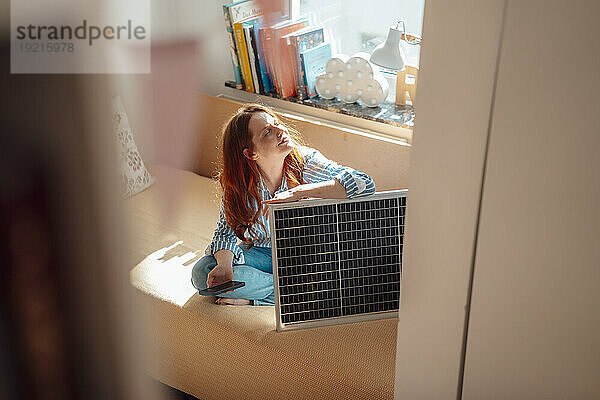 Frau sitzt mit Solarpanel und Smartphone zu Hause