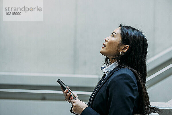 Geschäftsfrau schaut mit Smartphone am Arbeitsplatz nach oben