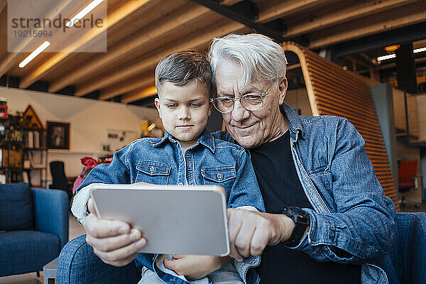 Lächelnder älterer Mann  der zu Hause einen Tablet-PC mit einem Jungen teilt