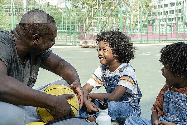 Vater und Kinder unterhalten sich auf dem Sportplatz