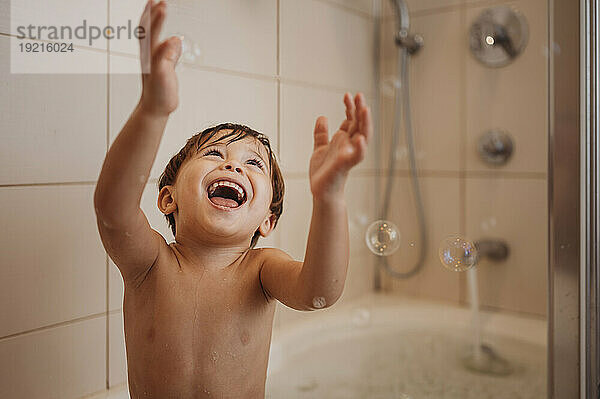 Fröhlicher Junge badet und genießt mit Seifenblasen in der Badewanne