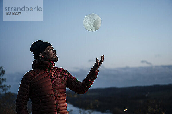 Reifer Mann wirft künstlichen Mond in die Luft unter dem Himmel