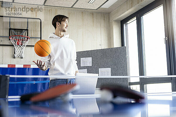 Junger Geschäftsmann spielt im Büro Basketball