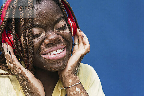 Lächelnde junge Frau mit kabellosen Kopfhörern vor blauem Hintergrund