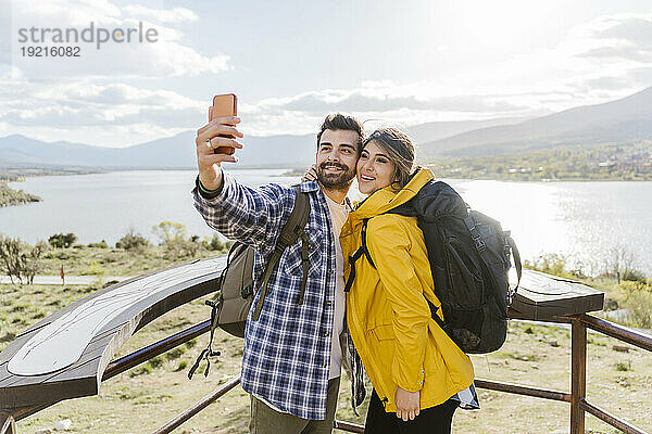 Lächelnder Tourist  der am Aussichtspunkt steht und ein Selfie mit dem Smartphone macht