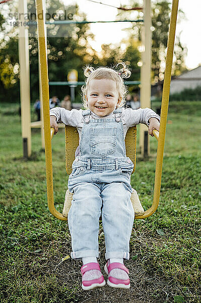 Smiling girl sitting on swing in park