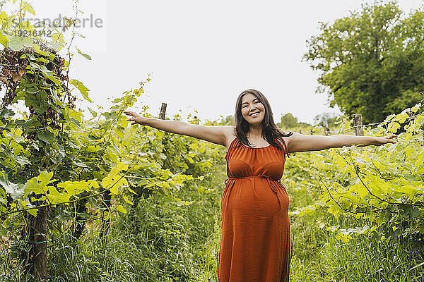 Happy pregnant woman with arms outstretched standing near plants