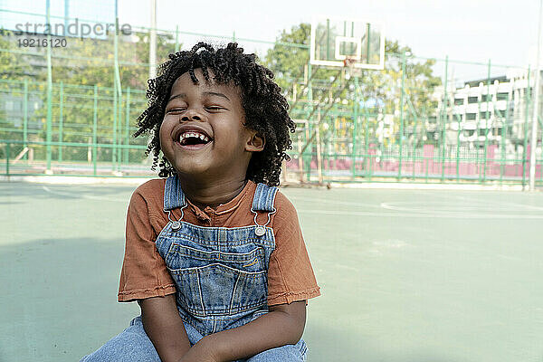 Junge mit lockigem Haar lacht auf Sportplatz