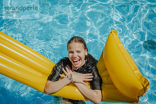 Cheerful girl leaning on airbed in swimming pool