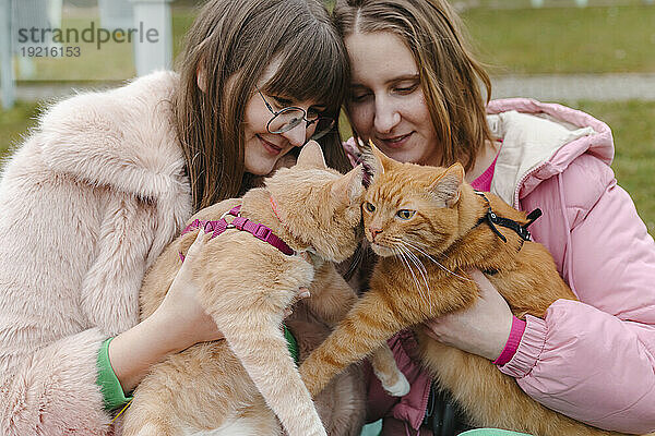 Lächelnde junge Frauen  die Katzen im Park tragen
