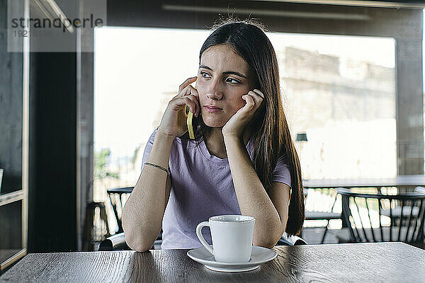 Portrait of pretty brunette talking on phone at cafe table