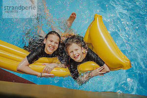 Cheerful friends leaning on airbed in swimming pool