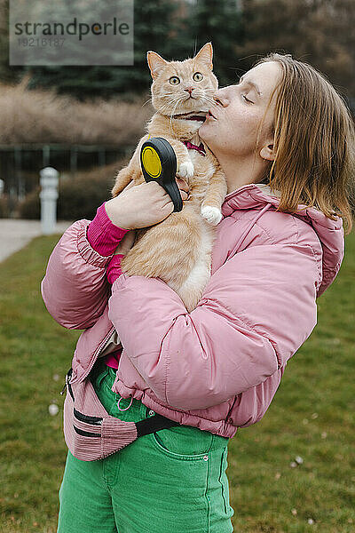 Junge Frau trägt und küsst Katze im Park