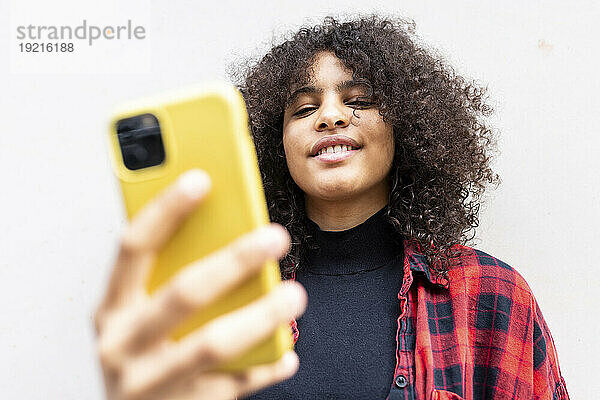 Lächelnde Frau macht Selfie mit Smartphone vor der Wand