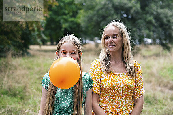 Lächelnde Mutter schaut Tochter zu  die im Park Luftballons bläst