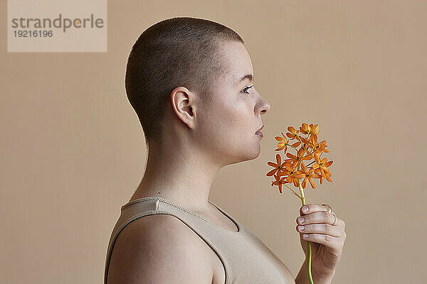 Woman with short hair smelling flower against beige background