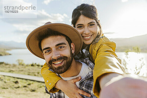 Lächelnde Frau macht Selfie mit ihrem Freund  der Hut trägt