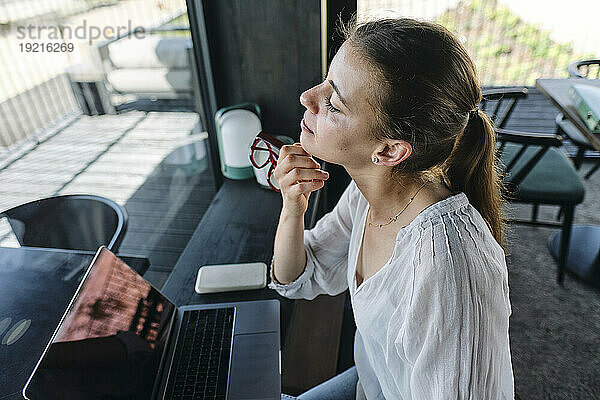Hübsche Blondine schaut durch das Fenster  während sie mit Laptop am Café-Tresen sitzt