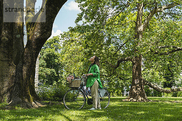 Frau mit Fahrrad steht am Wochenende neben Baum im Park