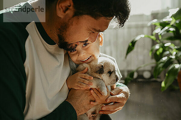 Smiling man holding son and cute puppy at home