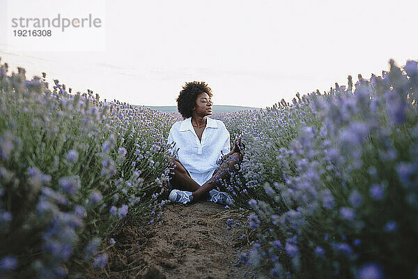 Junge Frau mit geschlossenen Augen meditiert im Lavendelfeld