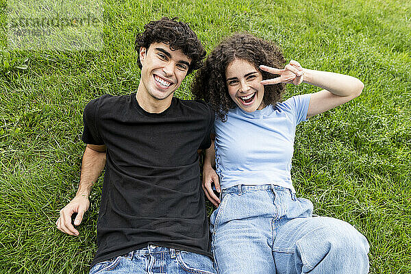 Smiling friend with woman gesturing peace sign on grass