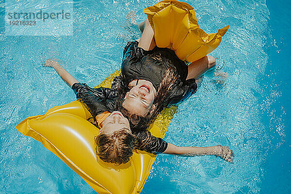 Friends lying on pool raft and floating over water at sunny day