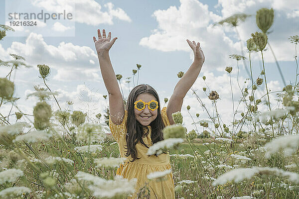 Glückliches Mädchen mit erhobenen Händen im Blumenfeld