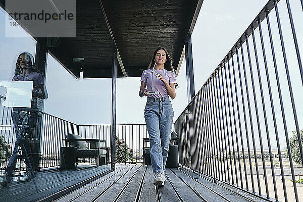 Young woman walking on balcony with model of wind turbine in hands