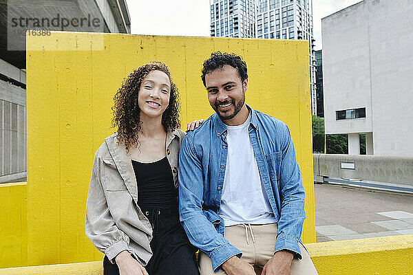Glückliches Paar sitzt vor gelber Wand
