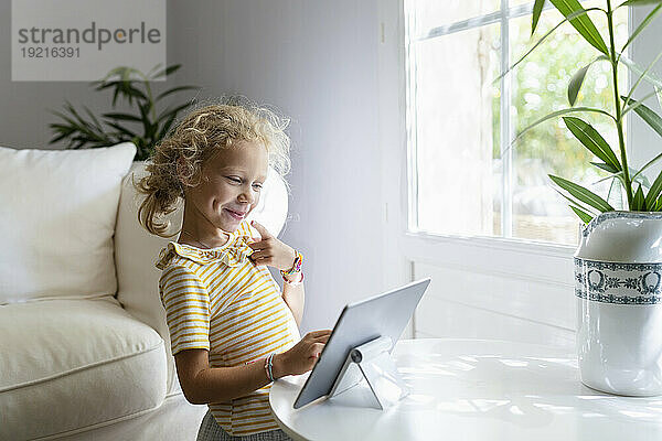Lächelndes Mädchen benutzt Tablet-PC auf dem Tisch im Wohnzimmer zu Hause