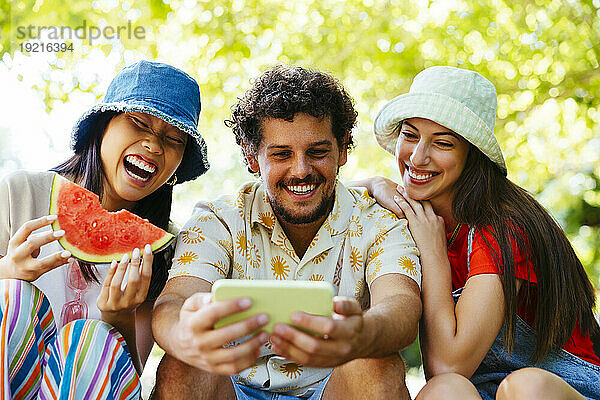 Lächelnder Mann benutzt Mobiltelefon mit Freunden