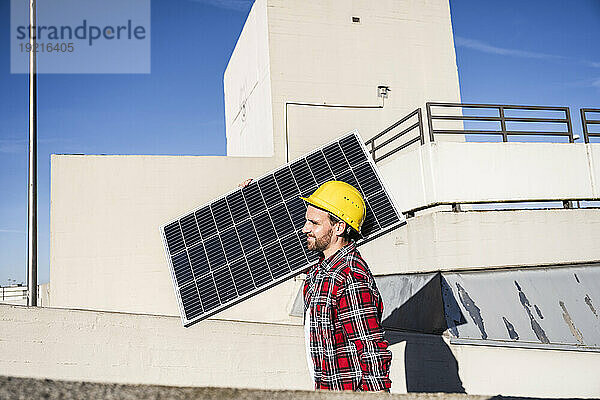 Ingenieur mit Schutzhelm und Solarpanel auf der Schulter