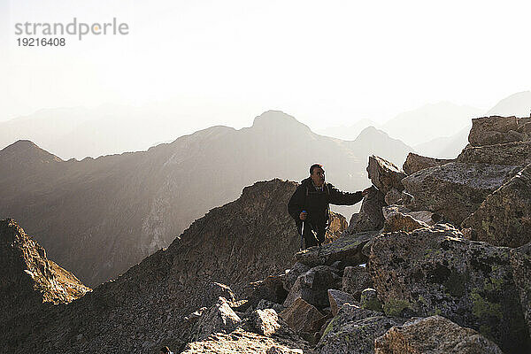 Reifer Mann wandert bei Sonnenaufgang auf einem felsigen Berg
