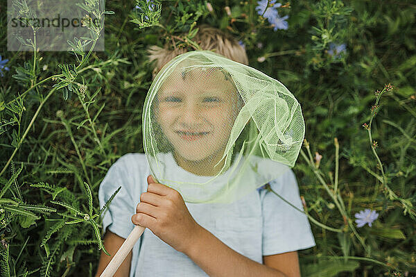 Lächelnder Junge hält Schmetterlingsnetz und liegt auf Pflanzen