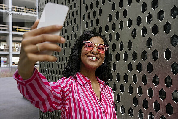 Glückliche Frau mit Sonnenbrille und Selfie mit Smartphone in der Nähe der Wand