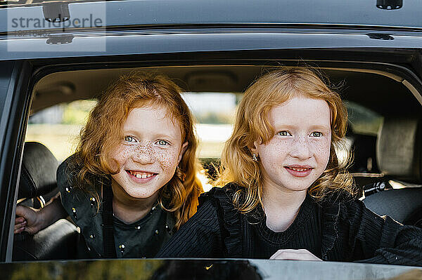 Lächelnde rothaarige Mädchen  die aus dem Autofenster schauen