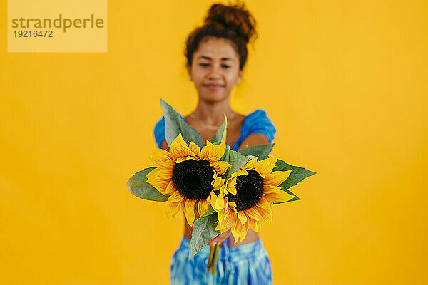 Frau mit einem Paar Sonnenblumen vor gelbem Hintergrund