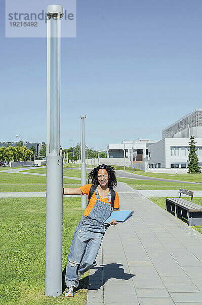 Lächelnder Student hält an einem sonnigen Tag eine Stange auf dem Campus