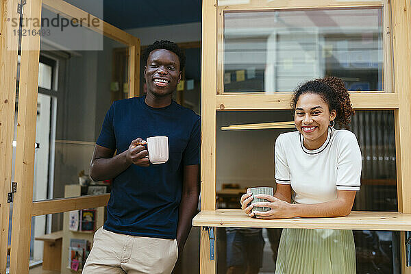 Fröhliche junge Studenten stehen mit einer Kaffeetasse im Türrahmen der Universität
