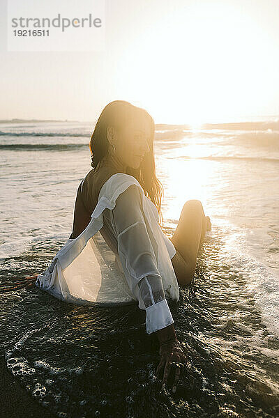 Frau sitzt im Meer am Strand