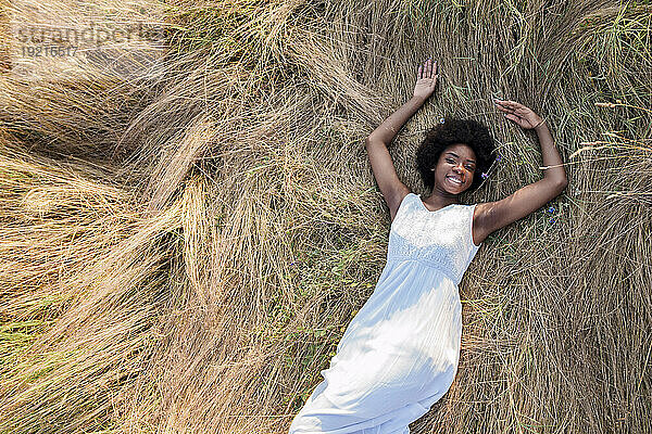 Happy young woman lying on dry grass in field