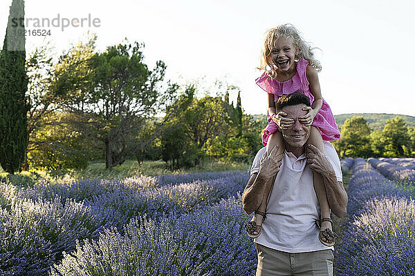 Fröhliches Mädchen  das die Augen bedeckt und Spaß mit seinem Vater im Lavendelfeld hat